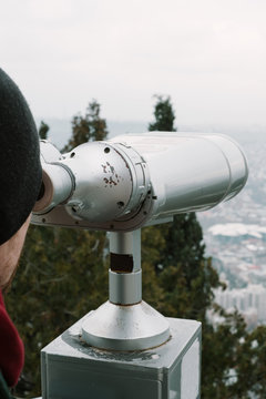 Young man looks through binoculars on a city