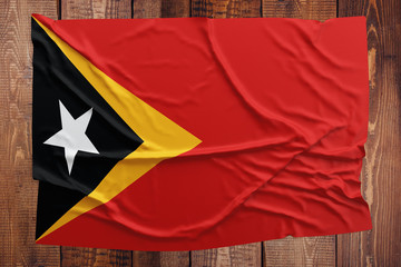 Flag of East Timor on a wooden table background. Wrinkled East Timorese flag top view.