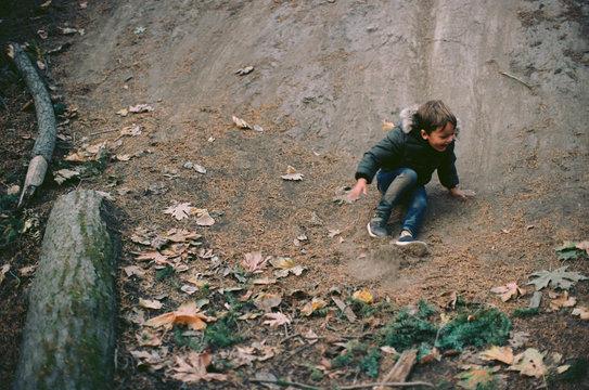 Adventure for young boy sliding down dirt hill in shady forest