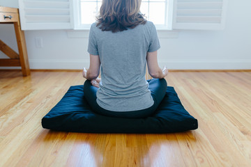 Woman sitting on a meditation cushion facing a window
