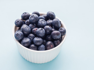 Fresh ripe blueberries in white bowl on a blue bright background
