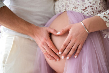 Parental love and happy motherhood. Closeup of heart shape on the background of a pregnant tummy.