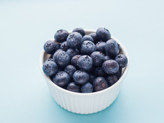 Fresh ripe blueberries in white bowl on a blue bright background
