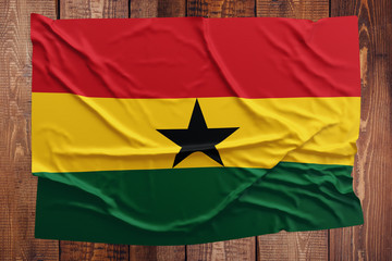 Flag of Ghana on a wooden table background. Wrinkled Ghanaian flag top view.