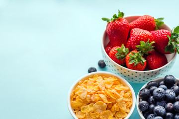 Concept of healthy gluten free breakfast with berries and corn flakes in the white bowls on a blue background, three plates, top view
