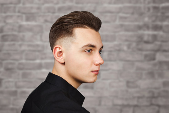 Young white guy with a pompadour hairstyle dressed in black shirt with a serious face on brick wall background