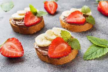 Delicious sandwiches with chocolate nougat, strawberry and banana. Concept of Breakfast. Dark concrete background.