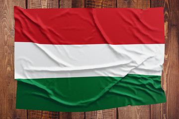 Fototapeta premium Flag of Hungary on a wooden table background. Wrinkled Hungarian flag top view.