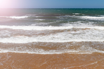 Ocean surf with sandy beach and turquoise water on a sunny summer day