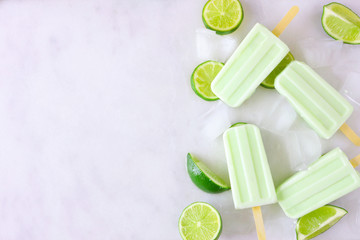 Lime yogurt popsicle side border, top view against a marble background with copy space