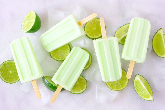 Healthy lime yogurt popsicles with lime slices scattered over a marble background