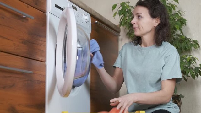 Washing clothes. A nice woman takes clean clothes out of the washing machine and smells them.