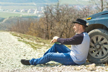 A man in a black hat take a book near the car