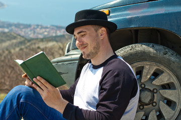 A man in a black hat take a book near the car