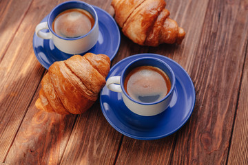two cups of coffee and croissants on a wooden background, good light, morning atmosphere