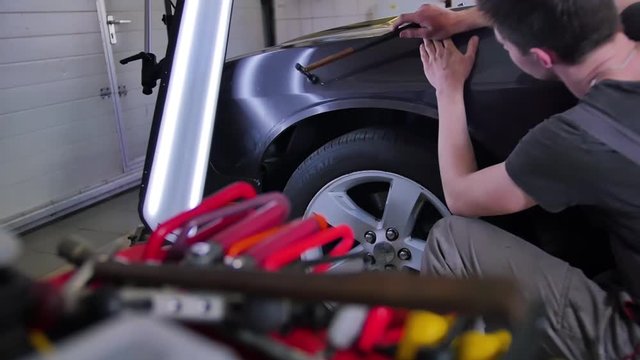 Dent Removal Tools. The young master aligns the dent with a hammer with rubber in a car repair shop. Bright colored instrument in the foreground, isolated, studio, auto, repair, technology.