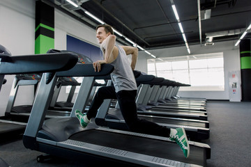 Young fit man in gym running on treadmill. Side view. Man running on treadmill in gym doing cardio workout
