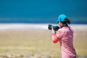 Landscape woman photographer taking photos in an amazing wilderness environment at Atacama Desert Andes mountains lagoons. A cut out silhouette over the blue waters with a mirror less camera shooting
