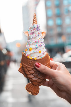 Soft Ice cream with Fish shaped waffle from Korean or Japan. Woman eating a delicious taiyaki outside in New York city. Unicorn decoration.