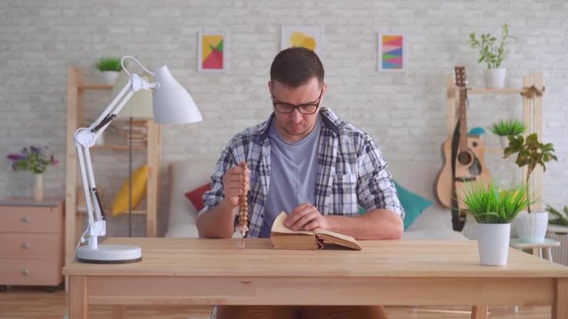Young man with glasses with a rosary in his hands and reading the Bible