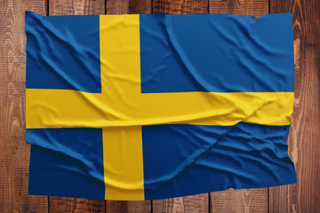 Flag of Sweden on a wooden table background. Wrinkled Swedish flag top view.