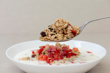 Una cuchara en un plato de cereales y fresas con leche.