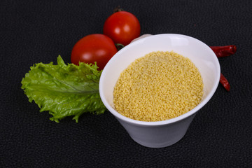 Raw couscous in the bowl served salad leaves, tomato and pepper