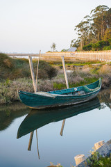 Obraz premium Quaint small boat next to shore in peaceful lagoon on bright day. Boat reflection on water.