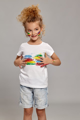 Beautiful little girl with a painted hands and cheeks is posing on a gray background.