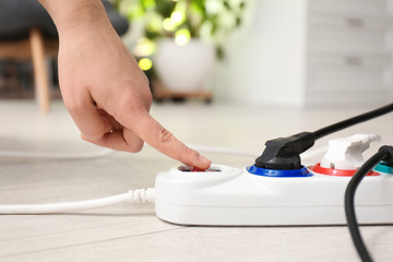 Woman pressing power button of extension cord on floor indoors, closeup. Electrician's professional...