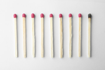 Row of whole matches and burnt one on white background, top view. Uniqueness concept