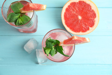 Glasses of grapefruit cocktails with ice on wooden table, flat lay