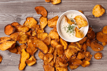 Sweet potato chips and bowl of sauce on wooden background, top view