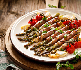 Grilled green asparagus wrapped in ham with the addition of aromatic herbs and spices on a white plate