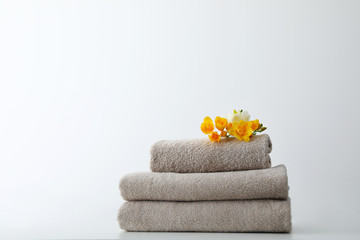 Stack of fresh towels with flowers on table against white background