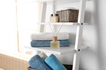 Shelving unit with clean towels and toiletries near white wall