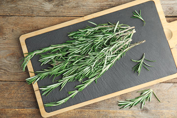 Board with fresh rosemary twigs on wooden table, top view