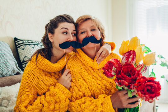 Senior mother and her adult daughter taking selfie with flowers using photo booth props at home. Mother's day concept.