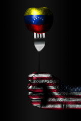 A hand with a drawn USA flag holds a fork, on which is a ball with a drawn Venezuela flag, a sign...