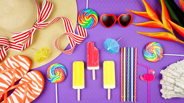 Summer vacation theme flatlay overhead with sunhat, lollipops, ice creams and sunglasses on purple background.