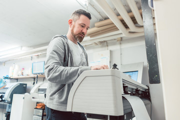 Mann bereitet den Großformatdrucker auf einen Druck vor - obrazy, fototapety, plakaty