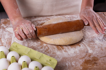 young woman in apron kneading dough on board