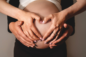Mom and dad mother and father couple making a hart shape hands holding over the pregnant woman belly waiting for baby son or daughter to be born