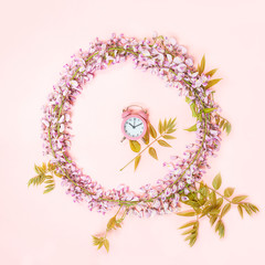 Circle frame of pink alarm clock and beautiful wisteria flowers branch with blossoms buds on pink background. Minimal beauty spring composition. Flat lay, top view.