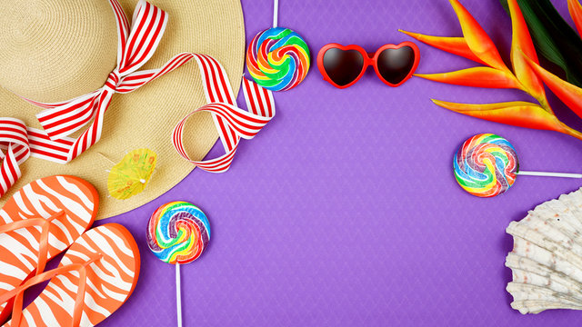 Summer vacation theme flatlay overhead with sunhat, lollipops, ice creams and sunglasses on purple background.