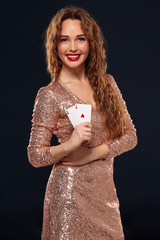 Pretty young brown-haired woman in golden cocktail dress holding pair of aces and smiling