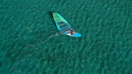 Aerial top view photo of fit man practising wind surfing in Mediterranean bay with crystal clear emerald sea