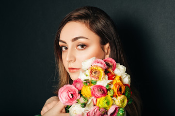 Studio close up portrait of beautiful young woman with long shiny hair, professional makeup, wearing white dress, holding colorful buttercup flowers