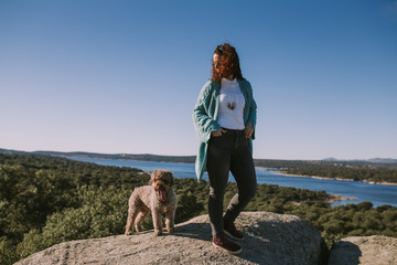 Young beautiful woman is looking at her dog in the middle of the nature. They are enjoying a pretty sun day.