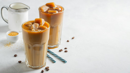 Ice coffee in a tall glass with cream poured over and coffee beans. Cold summer drink on a light background. With copy space